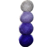 Stack of three felted balls in gray, purple, and blue on a blurred natural background