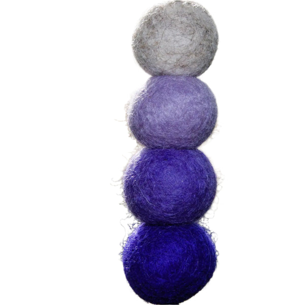 Stack of three felted balls in gray, purple, and blue on a blurred natural background