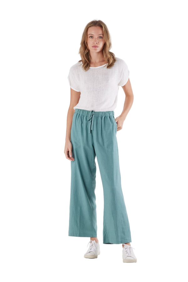 Woman wearing teal pants and a white top on a white background