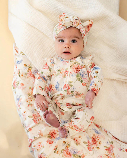 Baby in floral outfit and headband sitting on a textured surface