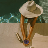 Person in a sun hat by a pool with a bottle and glass