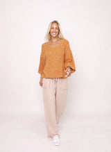 Woman wearing a mustard yellow sweater and beige pants on a white background