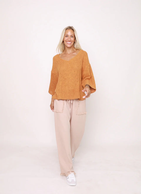 Woman wearing a mustard yellow sweater and beige pants on a white background