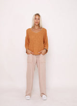 Woman wearing a mustard yellow sweater and beige pants on a white background