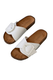 Pair of white sandals with brown soles on a stone pavement