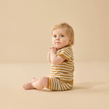 Baby wearing a yellow and brown striped outfit sitting on a beige background