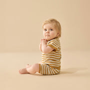 Baby wearing a yellow and brown striped outfit sitting on a beige background