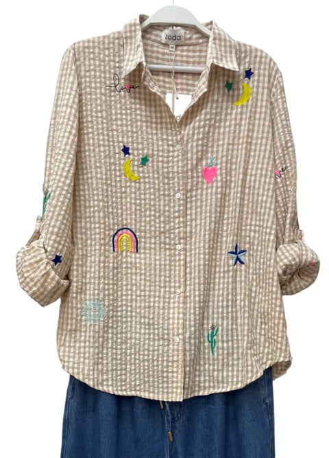 Beige checkered shirt with colorful embroidered designs on a white wooden background